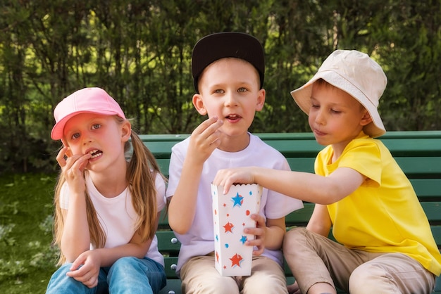 Tre bambini nel parco su una panchina che mangiano popcorn insieme alla famiglia degli amici