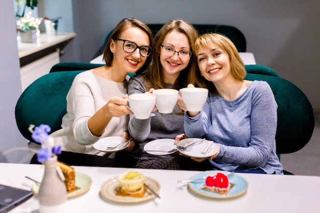 Tre belle ragazze caucasiche trascorrono del tempo insieme bevendo caffè nel caffè, divertendosi e mangiando torte e dessert.