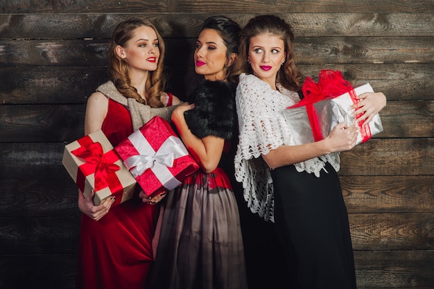 Tre belle ragazze con i regali di Natale in un fondo di legno