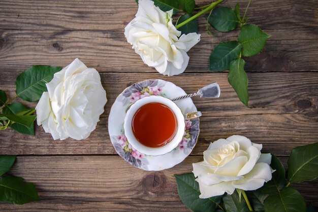 Tre belle rose bianche e una tazza di tè su un fondo di legno rustico