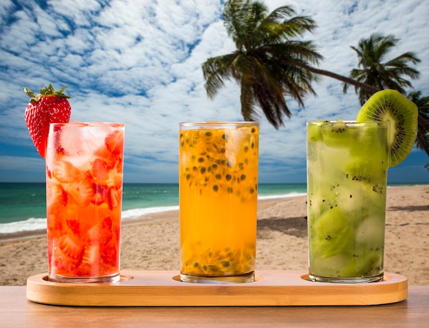 Tre bevande a base di frutto della passione, fragola e kiwi Caipirinha sullo sfondo della spiaggia