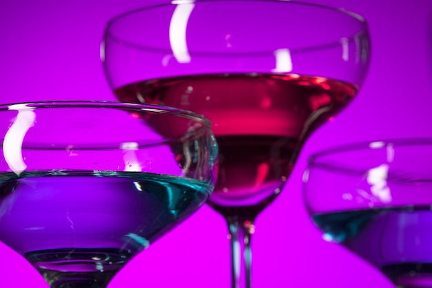 Tre bicchieri di vino farciti in piedi sul tavolo in studio. Illuminazione dai colori vivaci e luminosi. Trendy nel 2018 Lampadina Ultra Violetta. Decorazione d'arte con tono di colore mistico