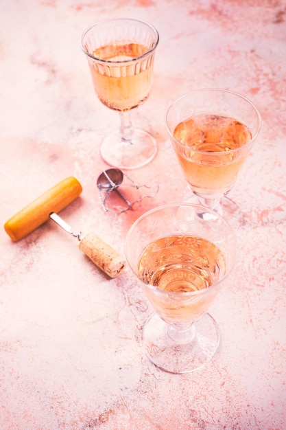 Tre bicchieri di vino rosato alla degustazione di vini con apribottiglie su fondo di marmo rosa