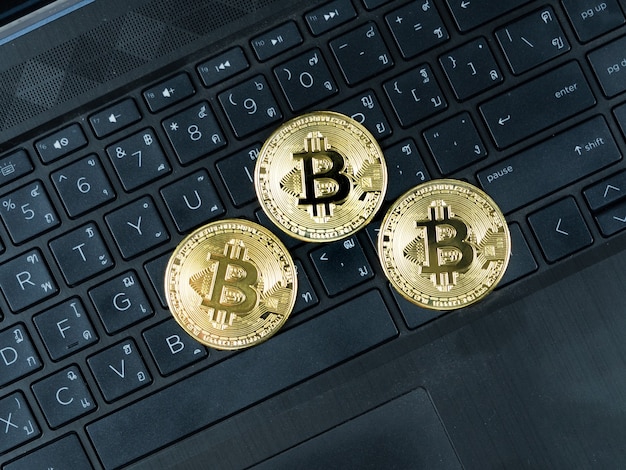 Tre bitcoin dorati sulla tastiera del computer portatile colorano di nero il concetto di criptovaluta di denaro digitale