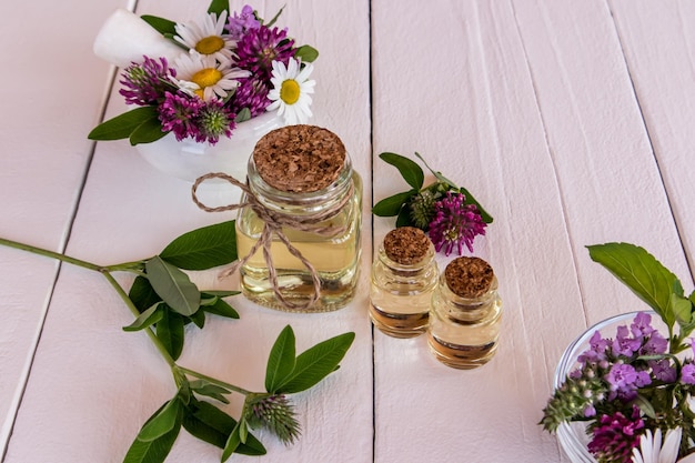 Tre bottiglie di vetro con olio l'essenza di erbe naturali su un tavolo di legno bianco tra fiori selvatici alternativa al fuoco selettivo della medicina