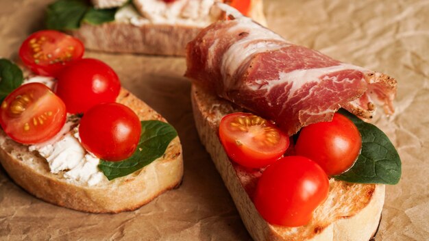 Tre bruschette fresche su carta artigianale. Un antipasto con ciabatta, formaggio, pomodori, pancetta e spinaci. Spuntino delizioso