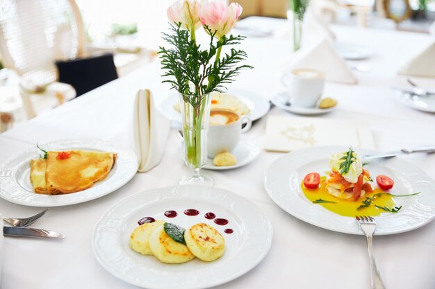 Tre cheesecake e frittelle su un piatto bianco con sfondo di marmellata di un vaso con fiori ristorante