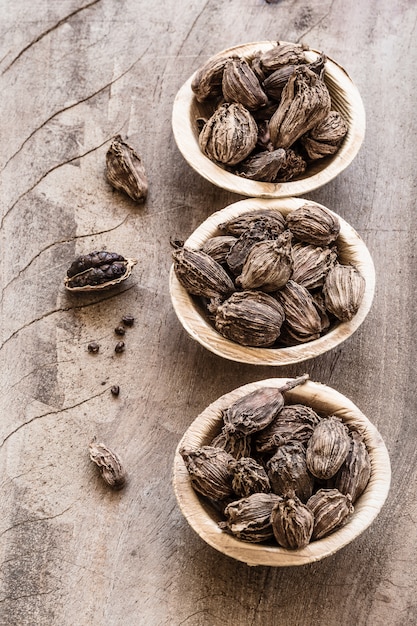 Tre ciotole con cardamomo nero su fondo di legno