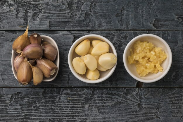 Tre ciotole di aglio intero e trasformato su un tavolo di legno. Una spezia popolare per la cucina.