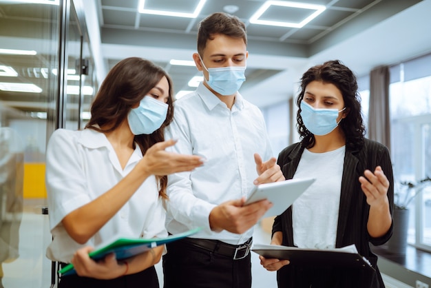 Tre colleghi di lavoro in maschera protettiva che discutono di questioni relative al lavoro in un ufficio.