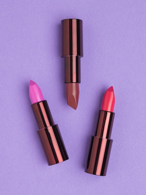 Tre colori di rossetto alla moda su una superficie viola. Decorazione delle labbra.