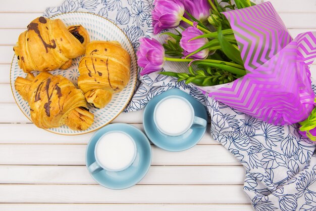 Tre croissant, due tazzine di caffè sul tavolo e un bouquet di bellissimi tulipani