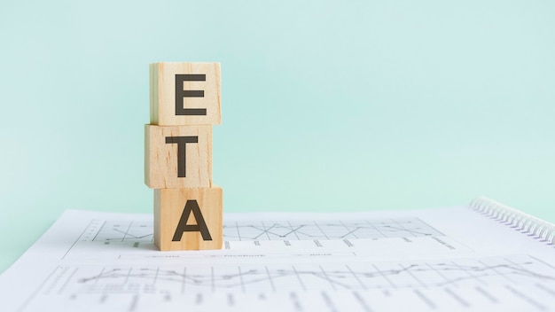 Tre cubi di legno con lettere ETA, su tavolo bianco e diagramma, concetto di affari. ETA - abbreviazione di TEMPO STIMATO DI ARRIVO