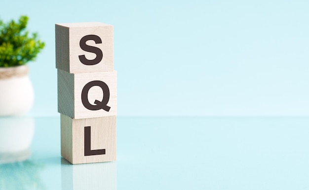 Tre cubi di legno con lettere - SQL - abbreviazione di linguaggio di query strutturato, su tabella blu, spazio per il testo a destra. Concetti di vista frontale, fiore sullo sfondo.