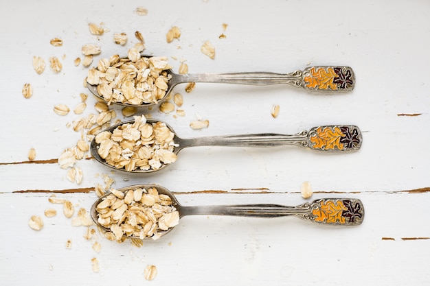 Tre cucchiai di farina d'avena che si trovano su un alimento sano di legno bianco.