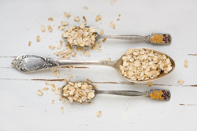 Tre cucchiai di farina d'avena che si trovano su un alimento sano di legno bianco.