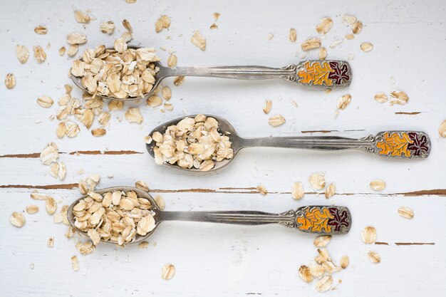 Tre cucchiai di farina d'avena che si trovano su un alimento sano di legno bianco.