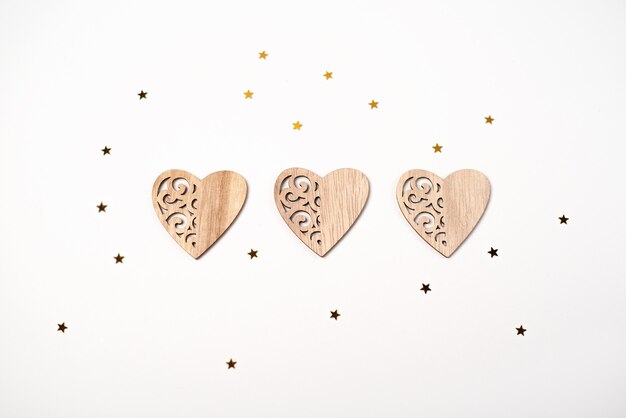 Tre cuori di legno e piccole stelle dorate su bianco. Concetto di San Valentino.