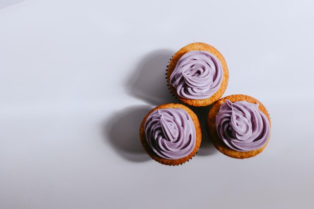 Tre cupcakes con glassa viola vista dall'alto sfondo bianco e ombre