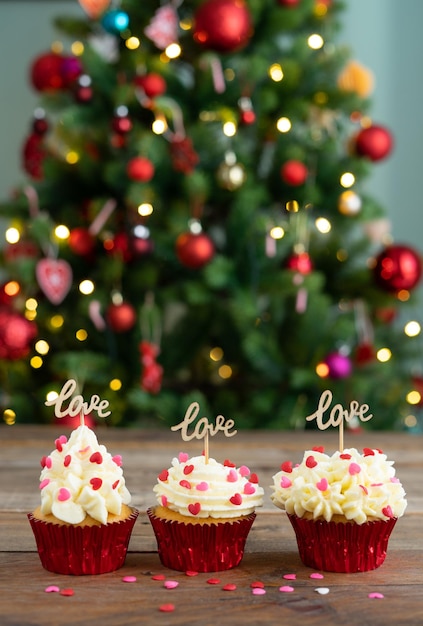 Tre cupcakes decorati su sfondo di legno con segno AMORE e albero di Natale Copia spazio Foto verticale