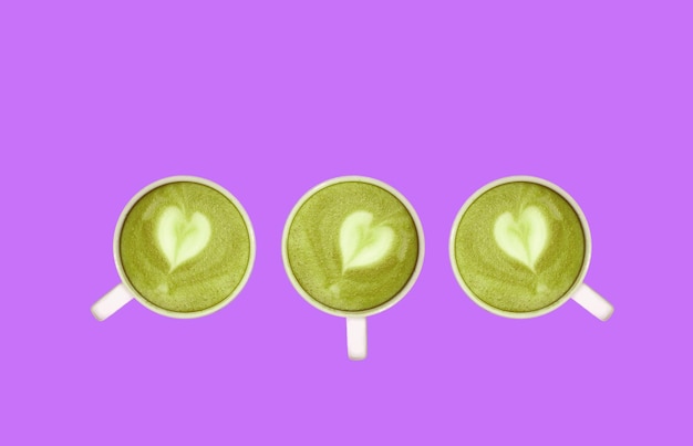 Tre di tè verde Matcha con latte art a forma di cuore remato su sfondo lilla