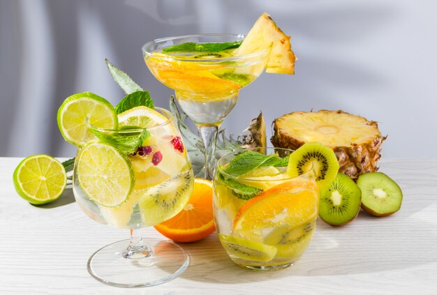 Tre diversi cocktail con frutta su un tavolo di legno chiaro.