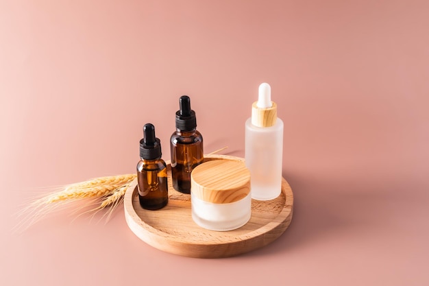 Tre diversi flaconi cosmetici con un contagocce con un rimedio naturale organico e un vasetto di crema su un vassoio rotondo in legno e uno sfondo beige