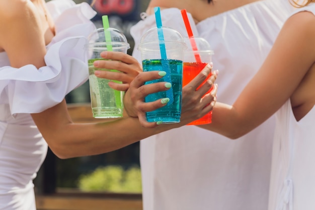 Tre donne che esultano con gustosi nettari con cubetti di ghiaccio con decorazioni di palme di cannucce nere in piscina trasparente acqua blu limpida pulita il sole splende pelle liscia abbronzata modalità spensierata festiva