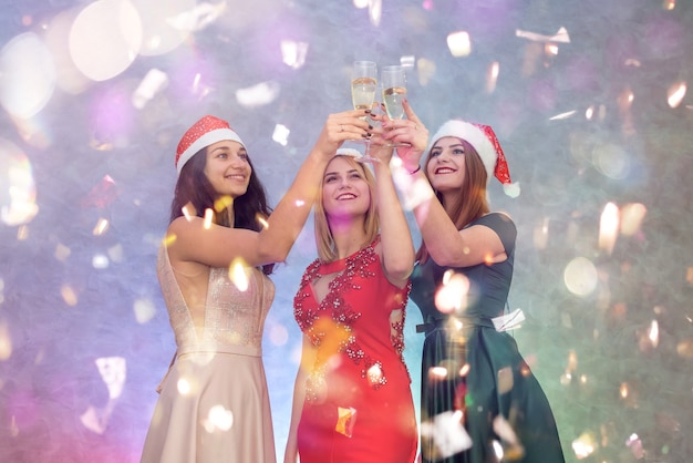 Tre donne in abiti eleganti e cappelli di Babbo Natale con bicchieri di champagne. Buon Natale concetto.