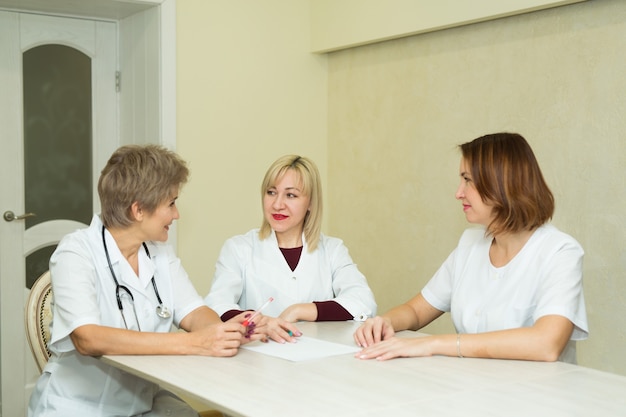 tre donne medico in camice bianco siedono al tavolo della clinica in ufficio