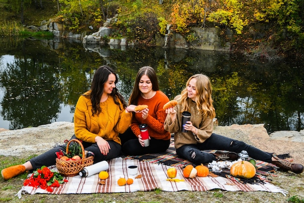 Tre donne migliori amiche al picnic autunnale nel parco. Plaid, thermos e décolleté colorati. Amici che si divertono all'aperto. Calda giornata autunnale di ottobre