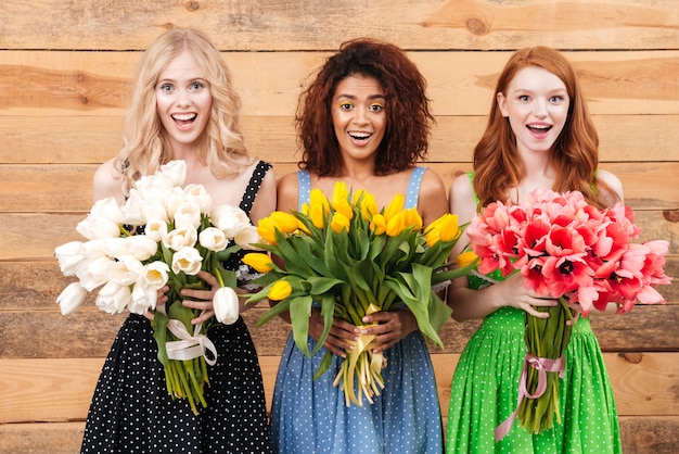 Tre donne sorprese che tengono i mazzi di fiori