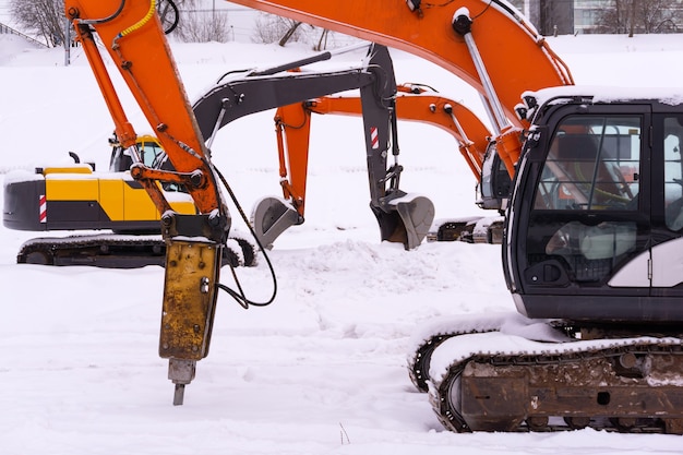 Tre escavatori cingolati multicolori sono parcheggiati su un campo innevato, bracci e bastoni formano un'infilata