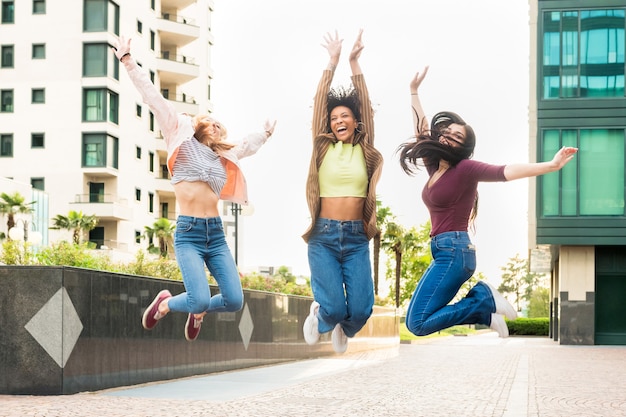 Tre esuberanti giovani donne felici che festeggiano saltando in aria insieme ridendo e applaudendo in una strada cittadina