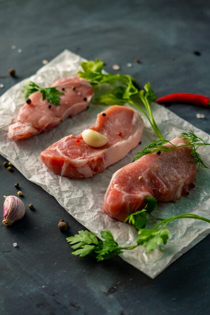 Tre fette di filetto su una carta da forno con spezie ed erbe su un tavolo nero