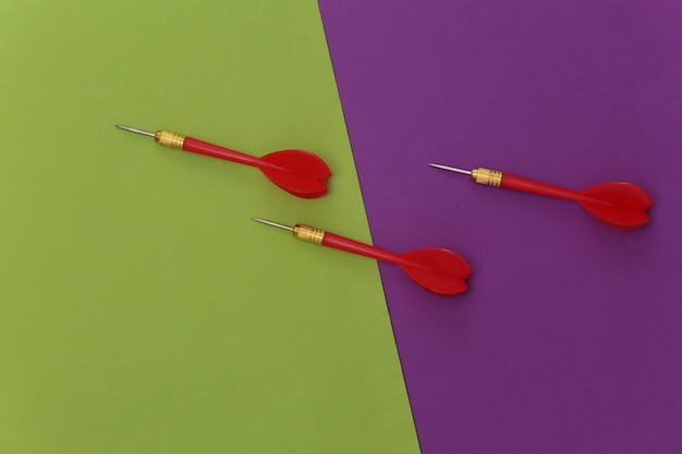 Tre freccette in plastica rossa con punta in metallo su sfondo verde viola.