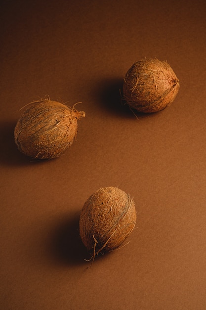 Tre frutti della noce di cocco su fondo normale marrone vibrante, concetto tropicale, vista di angolo