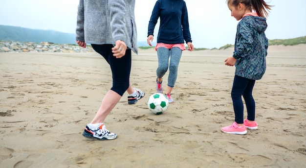 Tre generazioni di donne che giocano a calcio sulla spiaggia in autunno