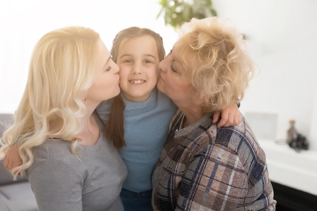 Tre generazioni di donne. La bella donna e l'adolescente stanno baciando la loro nonna mentre sono seduti sul divano a casa