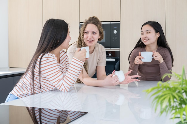 tre giovani amiche felici della diversità che bevono tè parlando divertendosi insieme alla cucina moderna