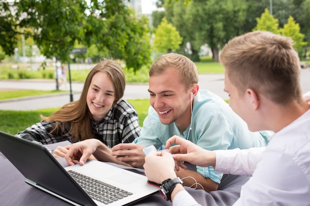 Tre giovani amici sorridenti felici che esaminano computer portatile nella regolazione all'aperto.