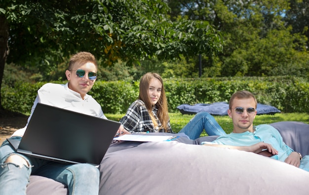 Tre giovani amici studenti che si rilassano all'aperto su un grande cuscino.