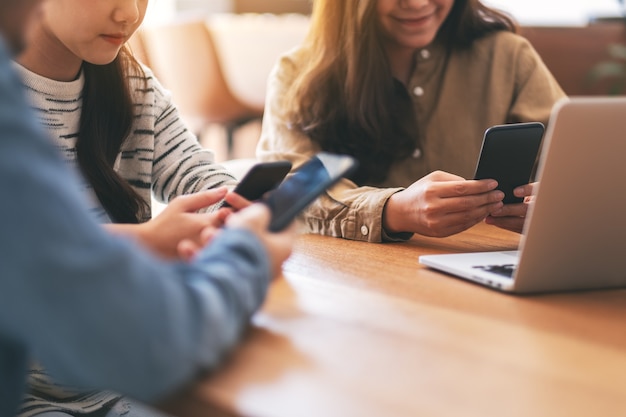 Tre giovani asiatici che usano e guardano il telefono cellulare e il computer portatile su un tavolo di legno