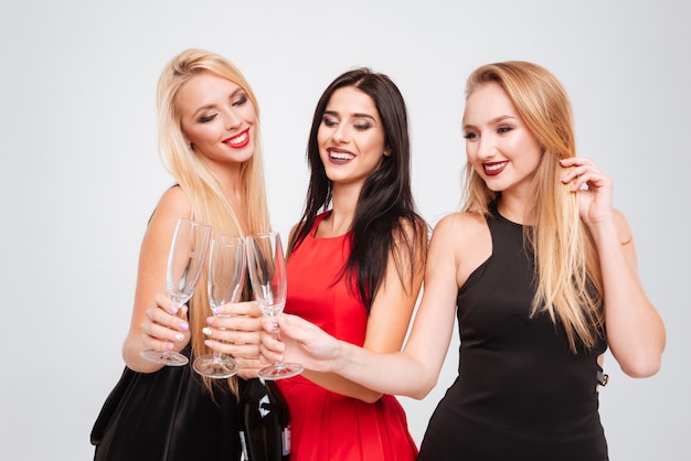 Tre giovani donne affascinanti felici che celebrano e bevono champagne insieme su sfondo bianco