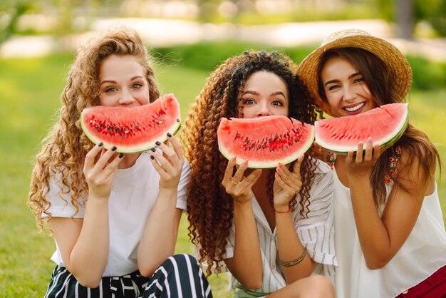 Tre giovani donne si divertono insieme e mangiano cocomero in una calda giornata estiva