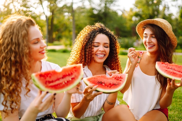 Tre giovani donne si divertono insieme e mangiano cocomero in una calda giornata estiva