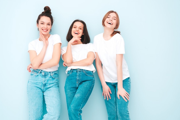 Tre giovani e belle donne hipster sorridenti nella stessa t-shirt bianca estiva alla moda e vestiti di jeans