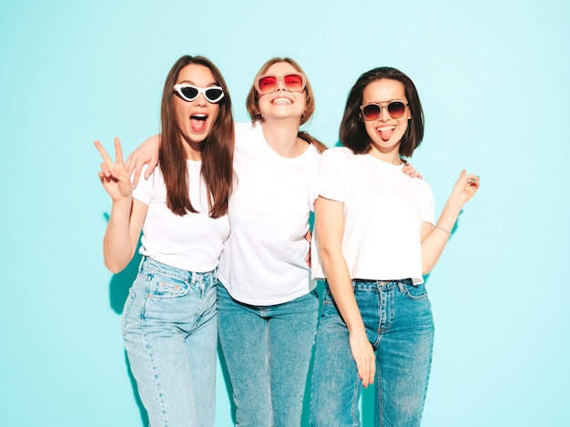 Tre giovani e belle donne hipster sorridenti nella stessa t-shirt bianca estiva alla moda e vestiti di jeans