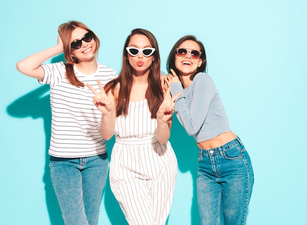 Tre giovani e belle donne hipster sorridenti nella stessa t-shirt bianca estiva alla moda e vestiti di jeans