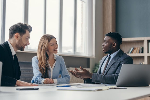 Tre giovani fiduciosi che hanno una riunione di lavoro mentre sono seduti insieme alla scrivania dell'ufficio